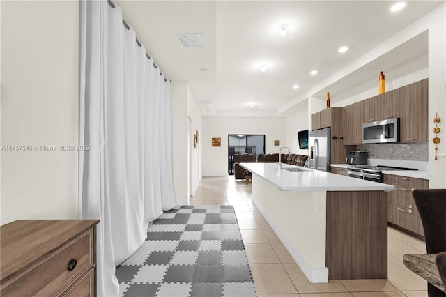 kitchen with light tile patterned floors, a center island with sink, visible vents, stainless steel appliances, and backsplash