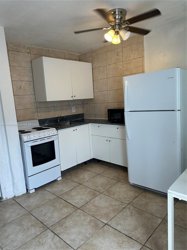 kitchen featuring light tile patterned flooring, white appliances, tile walls, white cabinets, and dark countertops