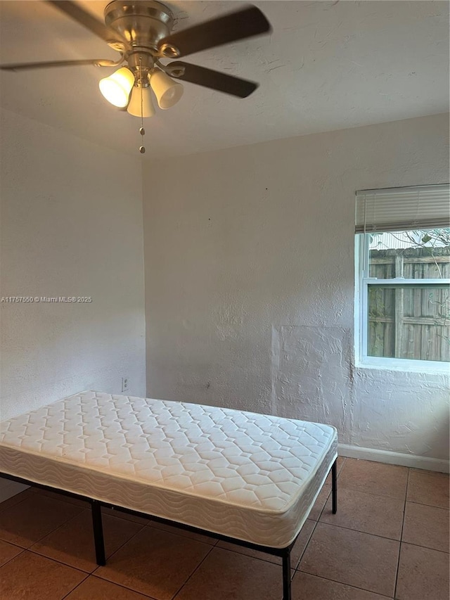 unfurnished bedroom featuring tile patterned flooring, baseboards, ceiling fan, and a textured wall