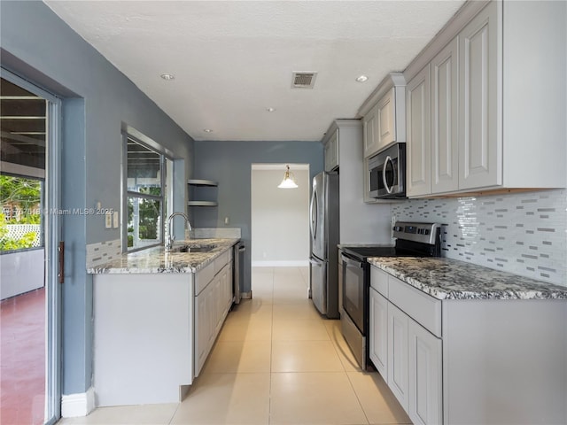 kitchen featuring light stone counters, stainless steel appliances, tasteful backsplash, visible vents, and a sink
