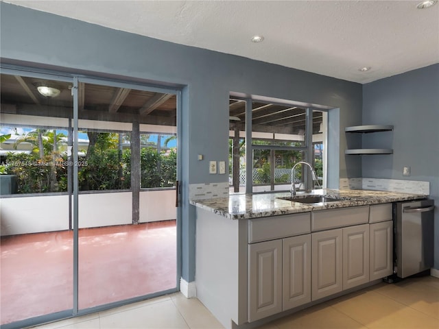 kitchen featuring light tile patterned floors, a sink, a wealth of natural light, and light stone countertops