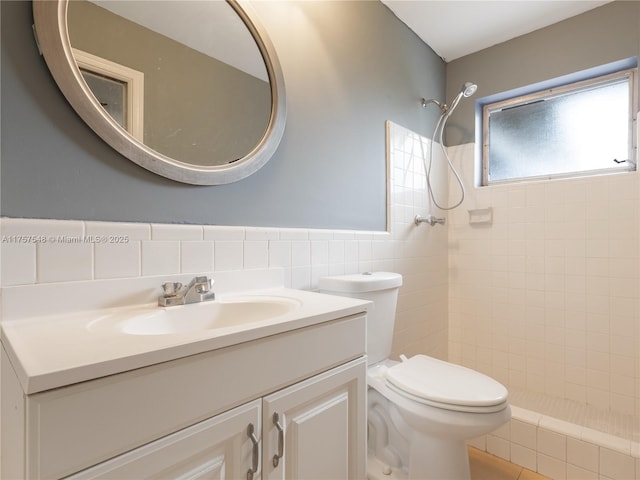 bathroom with tiled shower, toilet, a wainscoted wall, vanity, and tile walls