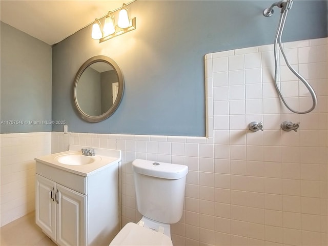 full bath featuring toilet, vanity, tile walls, and wainscoting