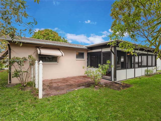 back of house featuring stucco siding, a patio area, a sunroom, and a yard
