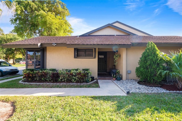 ranch-style home featuring stucco siding, a front yard, and a shingled roof