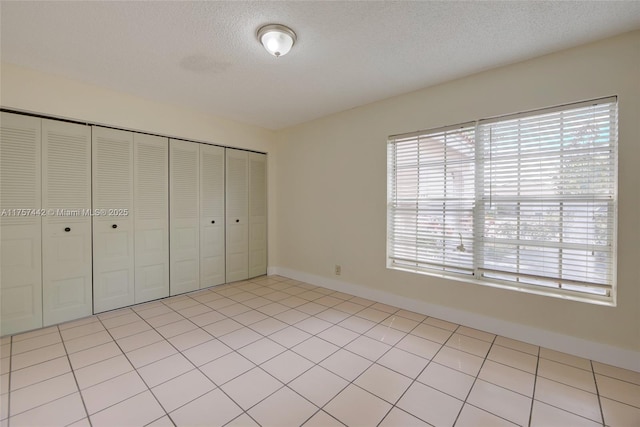 unfurnished bedroom featuring a closet, baseboards, a textured ceiling, and light tile patterned flooring