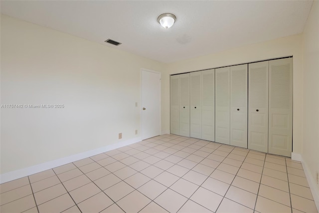 unfurnished bedroom featuring a closet, visible vents, baseboards, and light tile patterned flooring