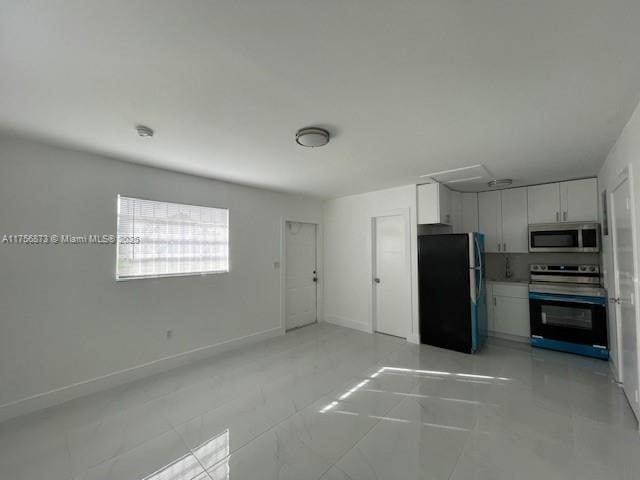 kitchen featuring baseboards, white cabinets, freestanding refrigerator, range, and stainless steel microwave