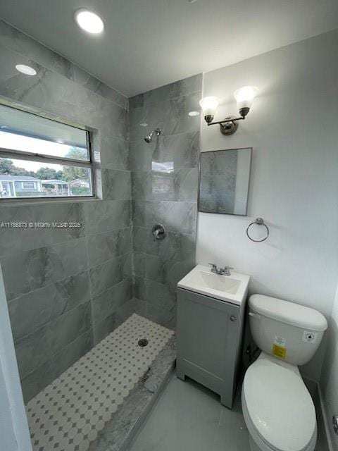 bathroom with toilet, a tile shower, and vanity