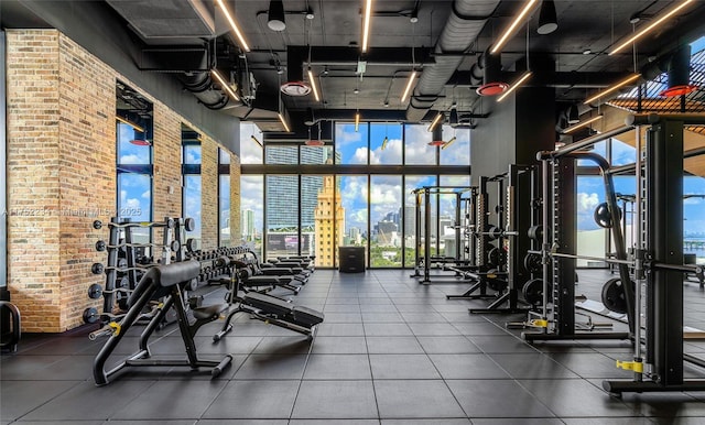 workout area with expansive windows, brick wall, and a view of city