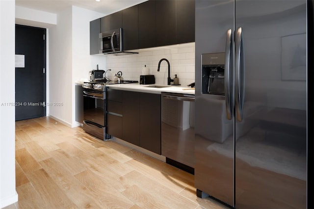 kitchen with tasteful backsplash, stainless steel appliances, light countertops, light wood-type flooring, and a sink