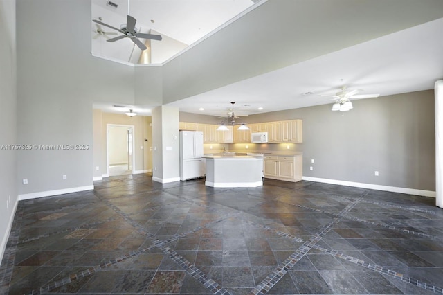 unfurnished living room featuring ceiling fan, a high ceiling, and baseboards