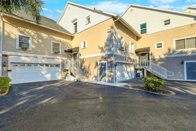 exterior space with a garage, aphalt driveway, stairway, and stucco siding