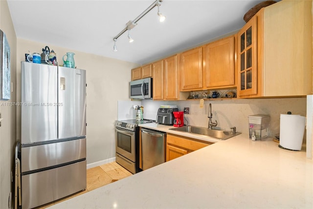 kitchen with stainless steel appliances, a sink, baseboards, light countertops, and glass insert cabinets