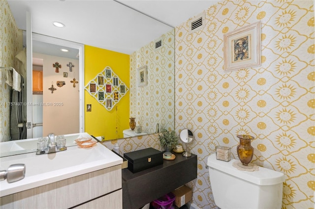 half bath with visible vents, vanity, toilet, and recessed lighting