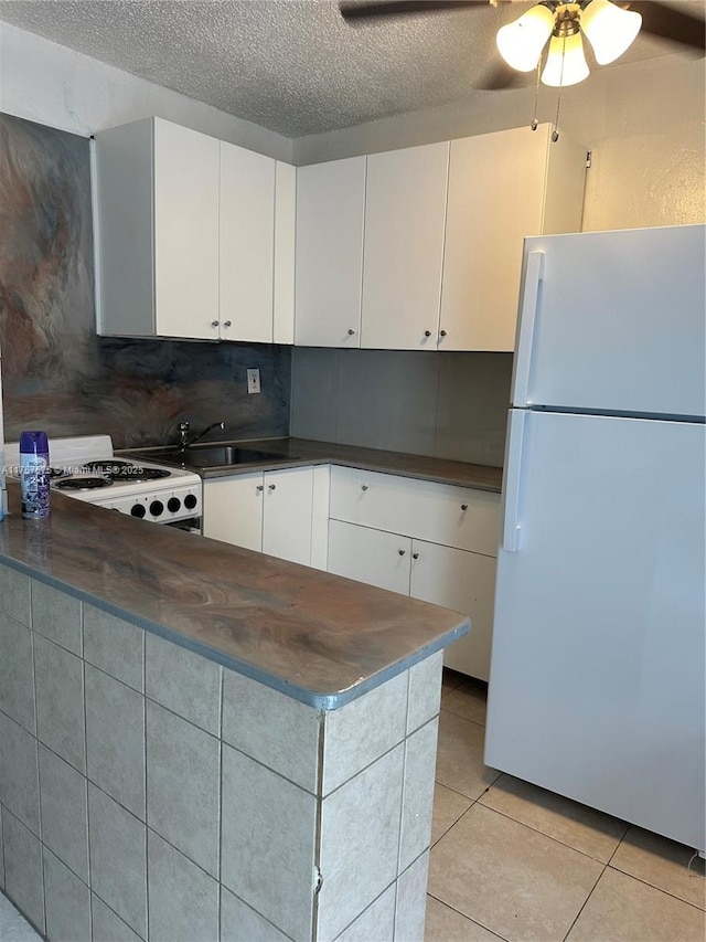 kitchen featuring dark countertops, white appliances, light tile patterned floors, and white cabinetry