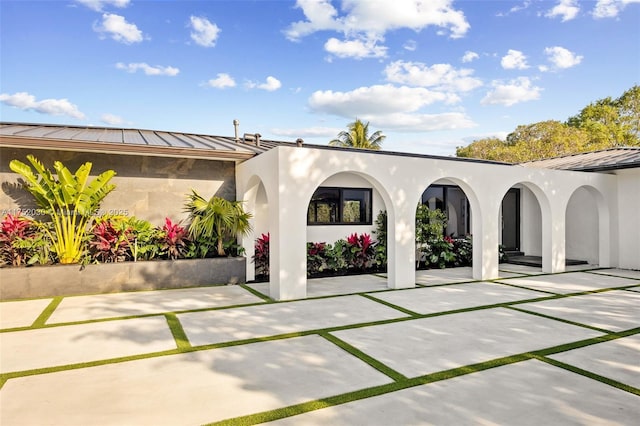 view of front of house featuring metal roof, a standing seam roof, a patio, and stucco siding