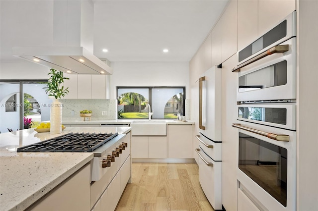 kitchen with light stone counters, island range hood, a sink, freestanding refrigerator, and light wood finished floors