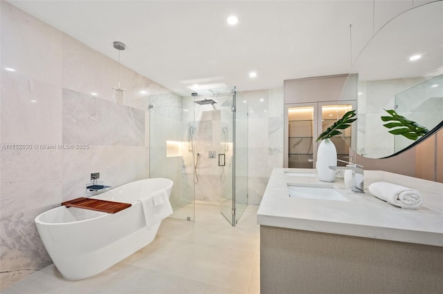 bathroom featuring a freestanding tub, a sink, tile walls, a marble finish shower, and double vanity