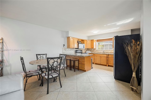 kitchen with light tile patterned floors, decorative backsplash, appliances with stainless steel finishes, a kitchen breakfast bar, and a peninsula