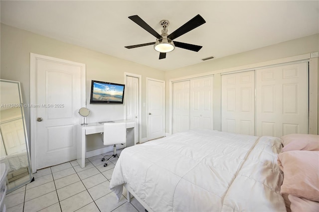 bedroom featuring light tile patterned floors, visible vents, ceiling fan, and multiple closets