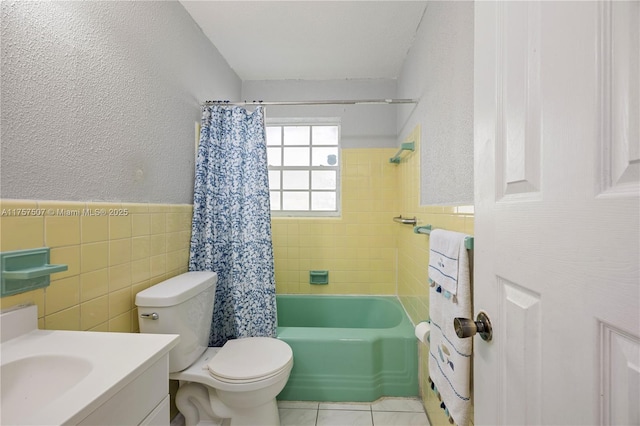 bathroom featuring tile patterned floors, toilet, tile walls, wainscoting, and a textured wall