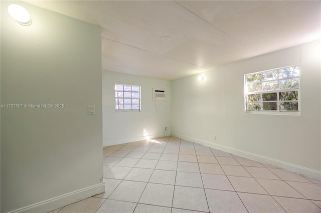 spare room with a wall unit AC, light tile patterned flooring, and baseboards