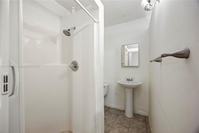 full bath with a textured ceiling, tile patterned floors, a sink, and walk in shower