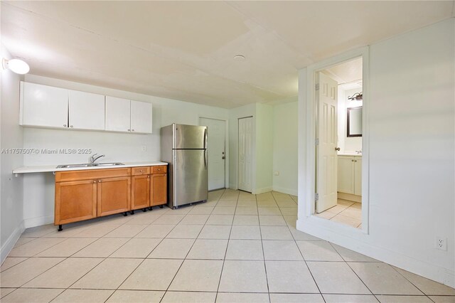 kitchen featuring a sink, light tile patterned floors, light countertops, and freestanding refrigerator