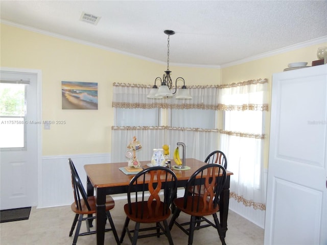 dining space with visible vents, ornamental molding, a notable chandelier, and wainscoting