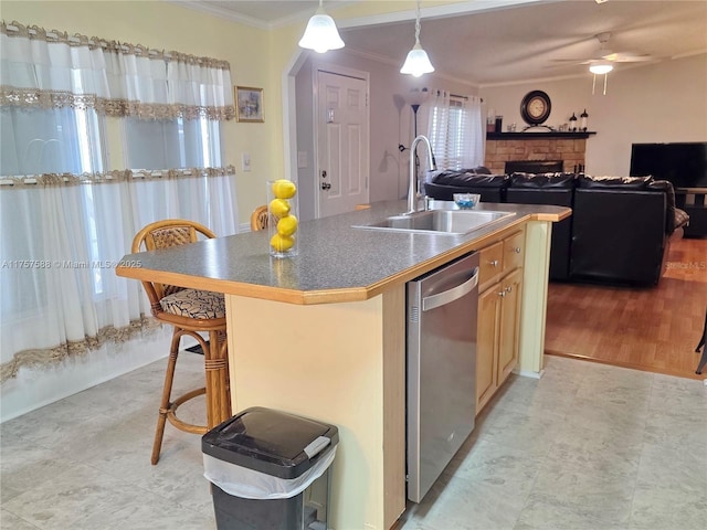 kitchen with a kitchen island with sink, stainless steel dishwasher, a fireplace, a sink, and ornamental molding