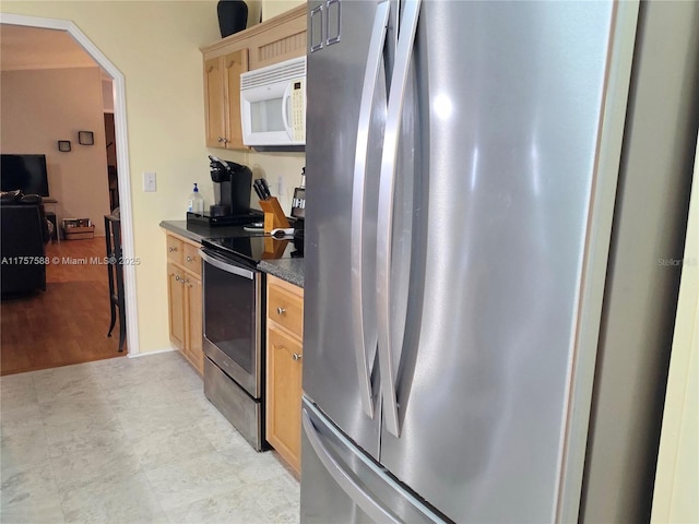 kitchen with arched walkways, appliances with stainless steel finishes, light brown cabinets, and dark countertops