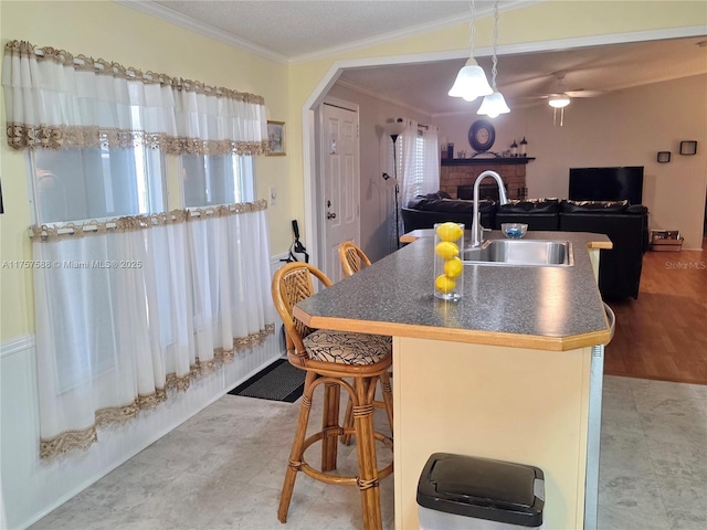 kitchen with dark countertops, a sink, a fireplace, a center island with sink, and ornamental molding