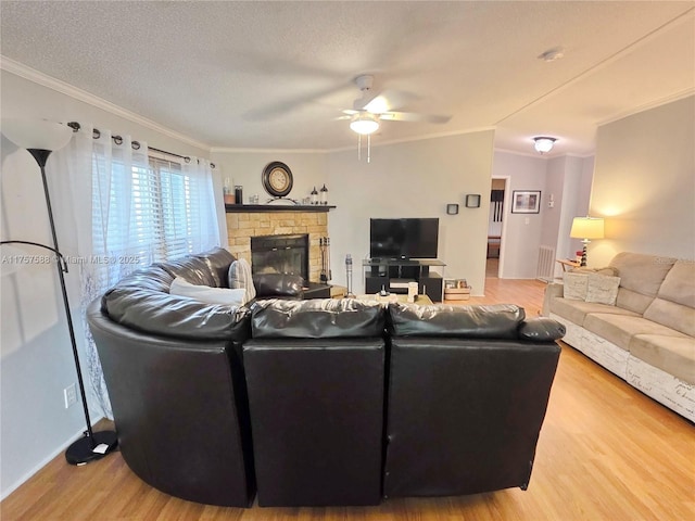 living room featuring ceiling fan, light wood finished floors, a fireplace, visible vents, and ornamental molding