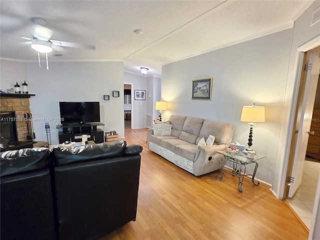 living room featuring visible vents, ornamental molding, a fireplace, light wood-style floors, and ceiling fan