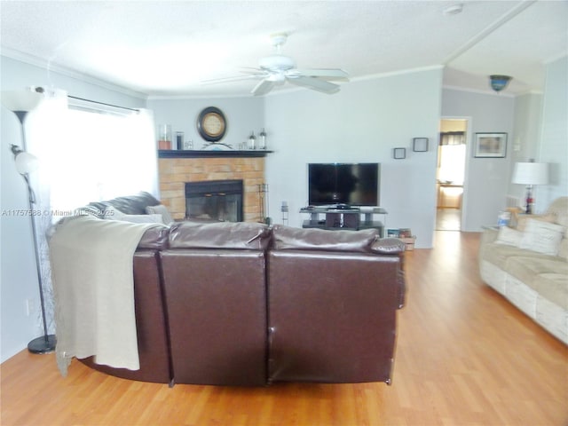 living area featuring ornamental molding, light wood-type flooring, a fireplace, and a ceiling fan