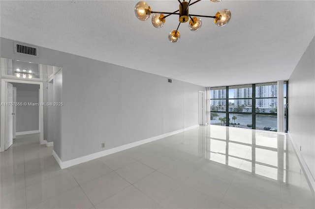 tiled spare room featuring baseboards, visible vents, an inviting chandelier, a textured ceiling, and floor to ceiling windows