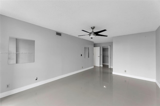 tiled empty room with ceiling fan, visible vents, baseboards, and a textured ceiling