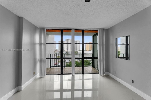 spare room featuring a city view, a textured ceiling, a wall of windows, tile patterned flooring, and baseboards