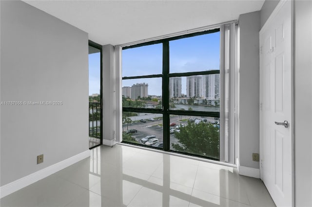 tiled empty room featuring a view of city, floor to ceiling windows, and baseboards