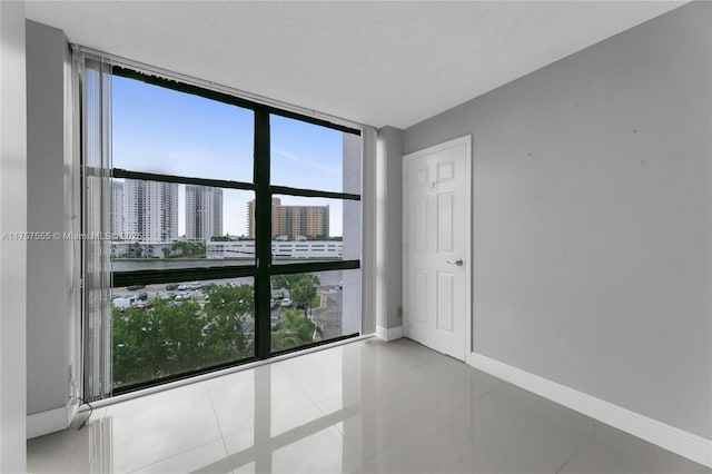 spare room with a view of city, baseboards, expansive windows, and tile patterned floors