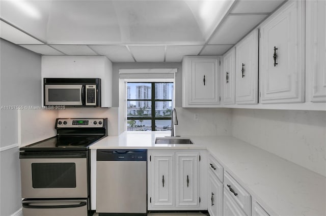 kitchen featuring light stone counters, appliances with stainless steel finishes, white cabinets, a sink, and a drop ceiling