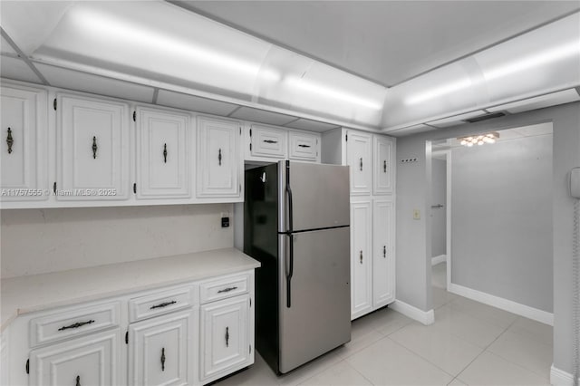 kitchen with light tile patterned floors, light countertops, freestanding refrigerator, and white cabinets