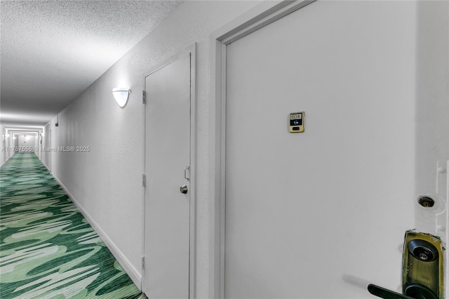 corridor with a textured ceiling, a textured wall, and baseboards