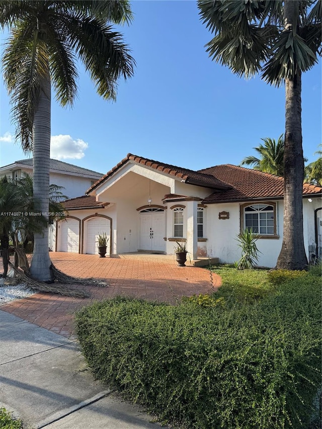 mediterranean / spanish-style house with an attached garage, a tile roof, and stucco siding