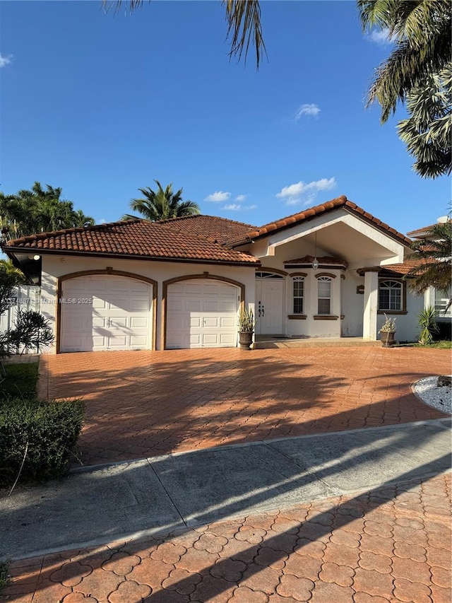 mediterranean / spanish-style home featuring a garage, a tile roof, and stucco siding