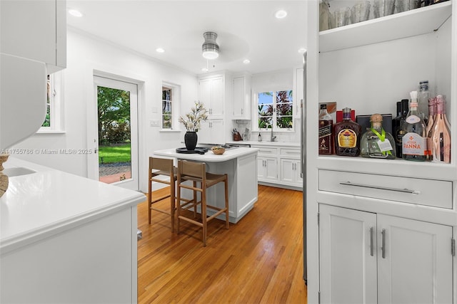 kitchen featuring recessed lighting, light countertops, light wood-style flooring, white cabinetry, and a sink