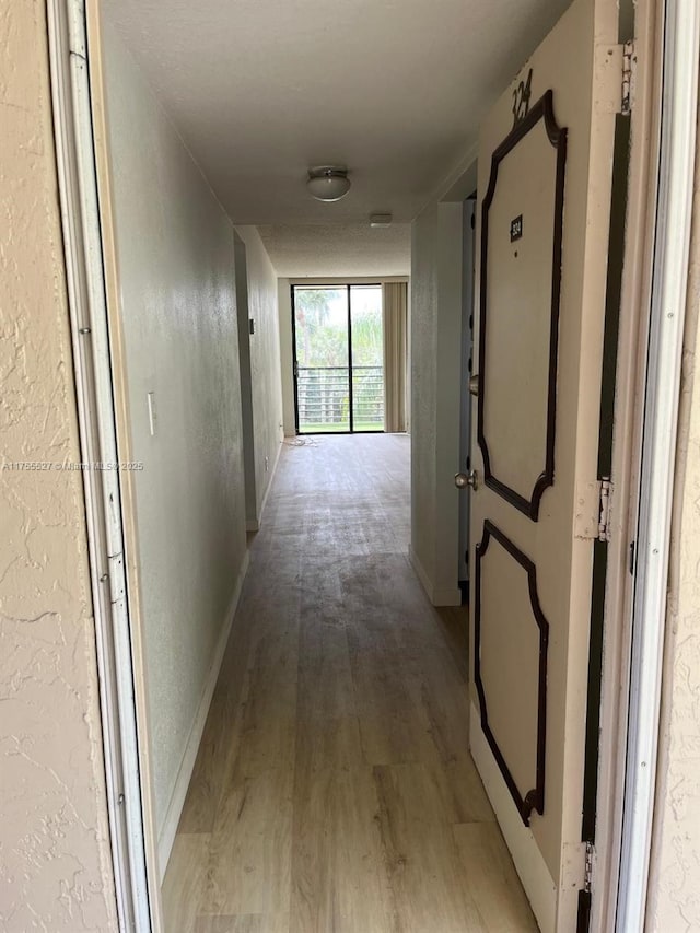 hall featuring light wood-style floors, baseboards, and a textured wall