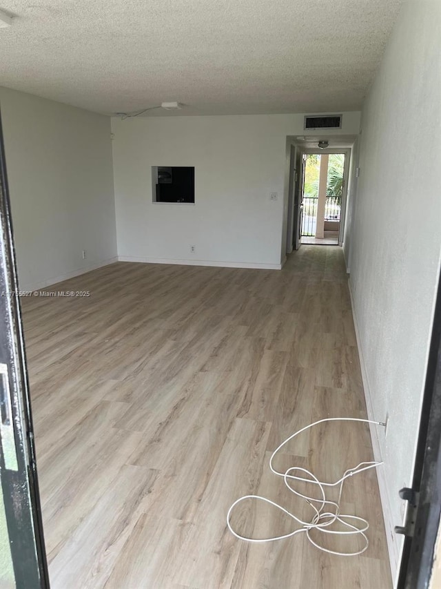 unfurnished room with a textured ceiling, wood finished floors, and visible vents