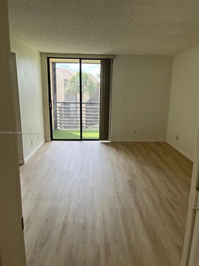 empty room featuring light wood-style flooring, a textured ceiling, floor to ceiling windows, and baseboards